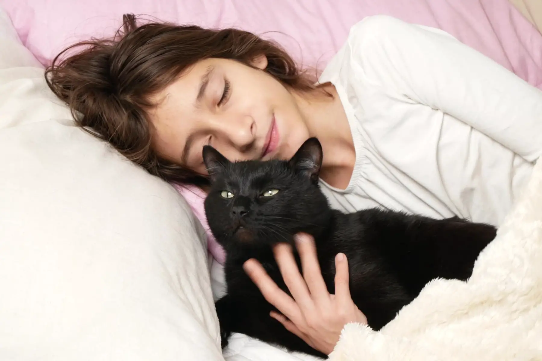 Svart katt väcker sin unga matte i sängen på ett kärleksfullt sätt